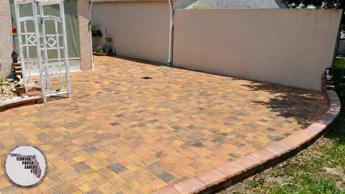 Curved tan paver patio beside a home and garden trellis