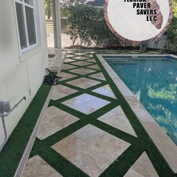Artificial turf strips framing geometric travertine pavers beside a swimming pool