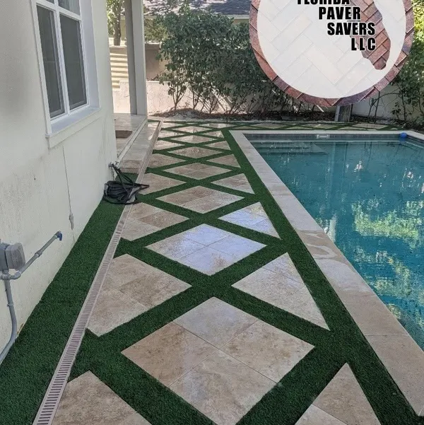 Artificial turf strips framing geometric travertine pavers beside a swimming pool