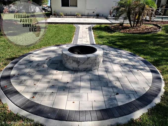 Round fire pit patio with a dark border and a path leading toward the home