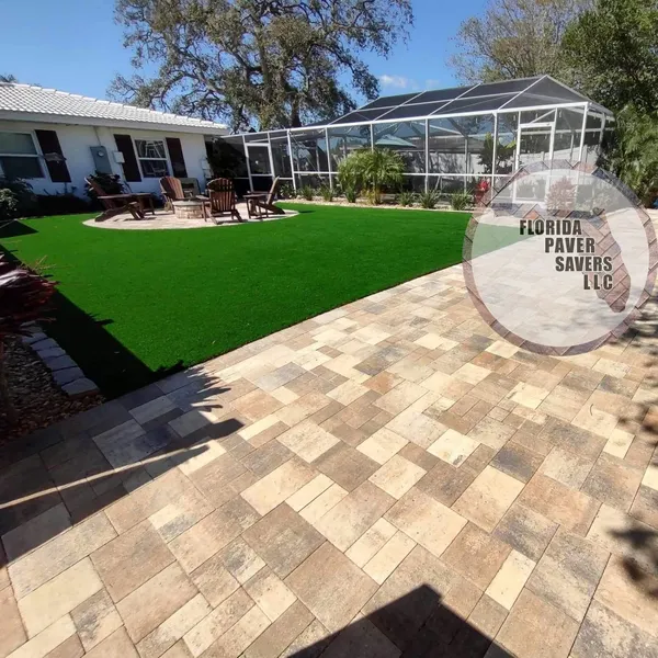 Artificial turf courtyard bordered by multicolor pavers beside a screened pool in Spring Hill