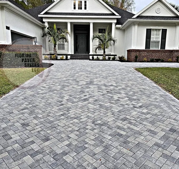 Broad gray paver driveway leading to the entrance of a white home