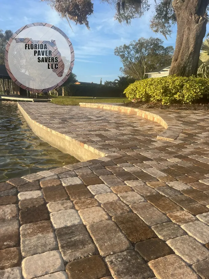 Raised curved paver patio beside a waterfront lawn and planted tree