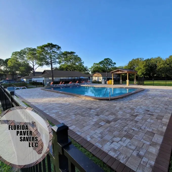Wide multicolor paver pool deck beside a lawn and open-air pavilion