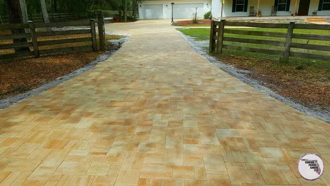 Long tan paver driveway passing between wooden fences